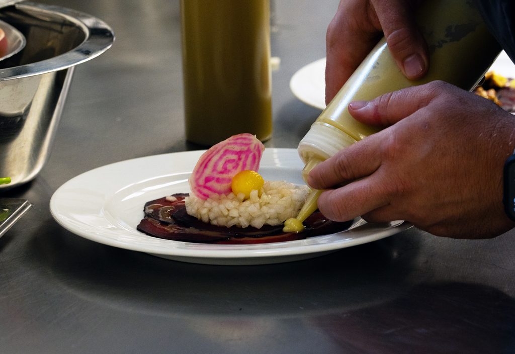 Beim Kochworkshop "Vegan Cooking" gibt jemand Soße auf einen Teller mit Rote Bete und anderen Zutaten.